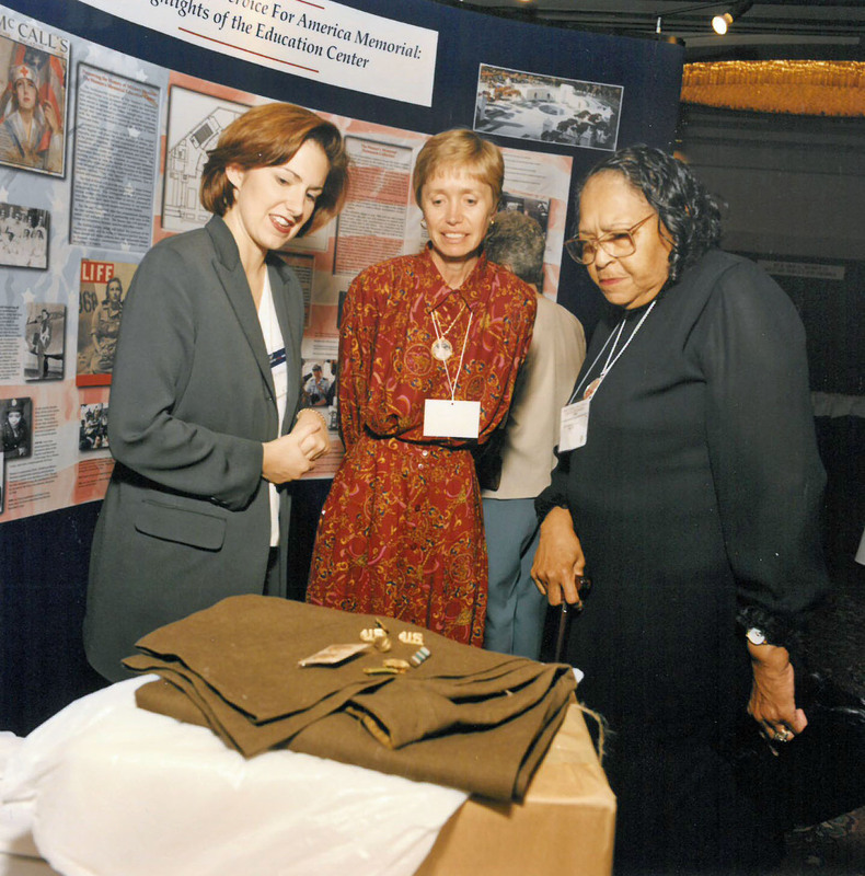 Three women in formal attire looking at a women's military uniform