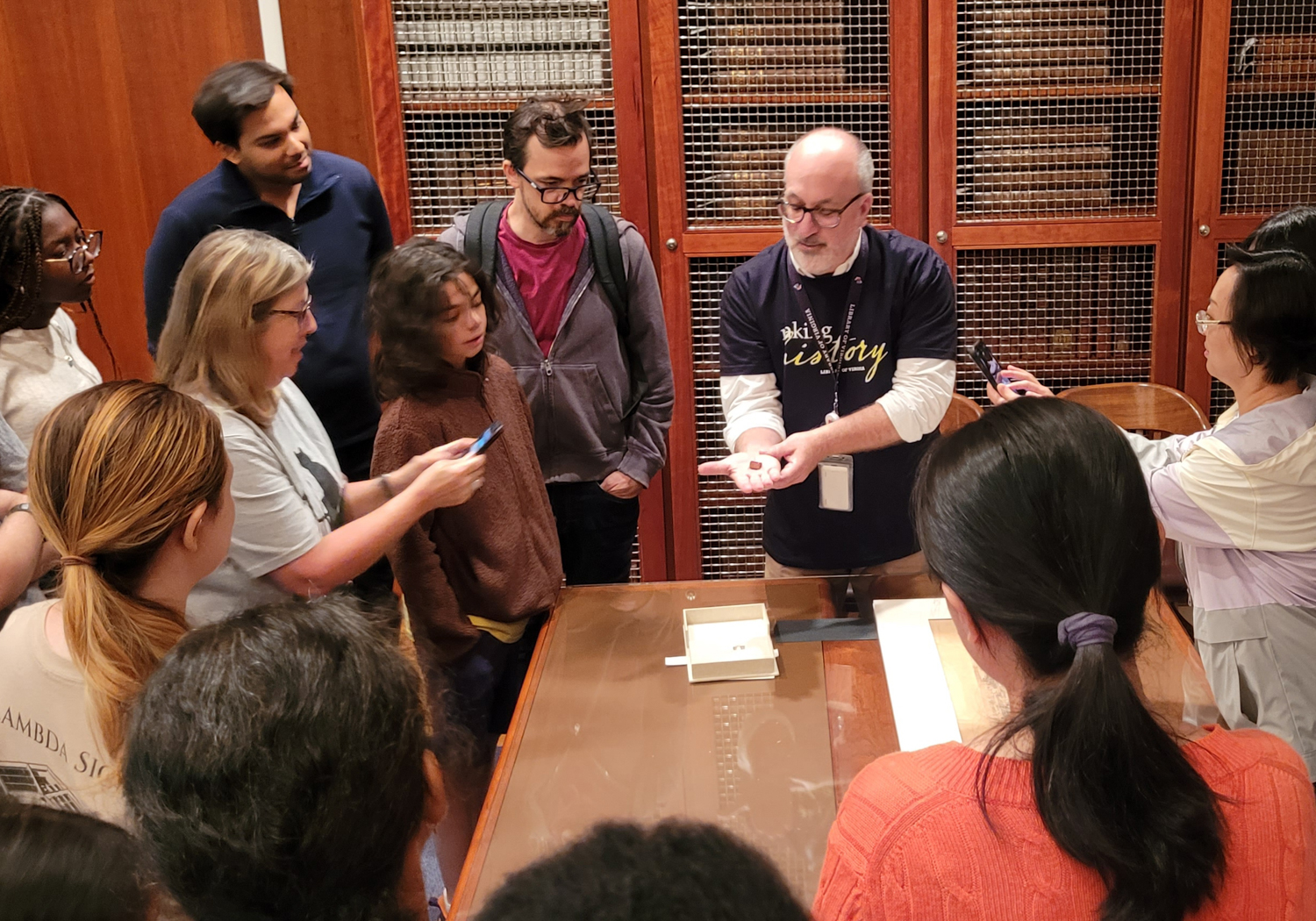 A library staff member shows a tour group a tiny book in the palm of his hand. 