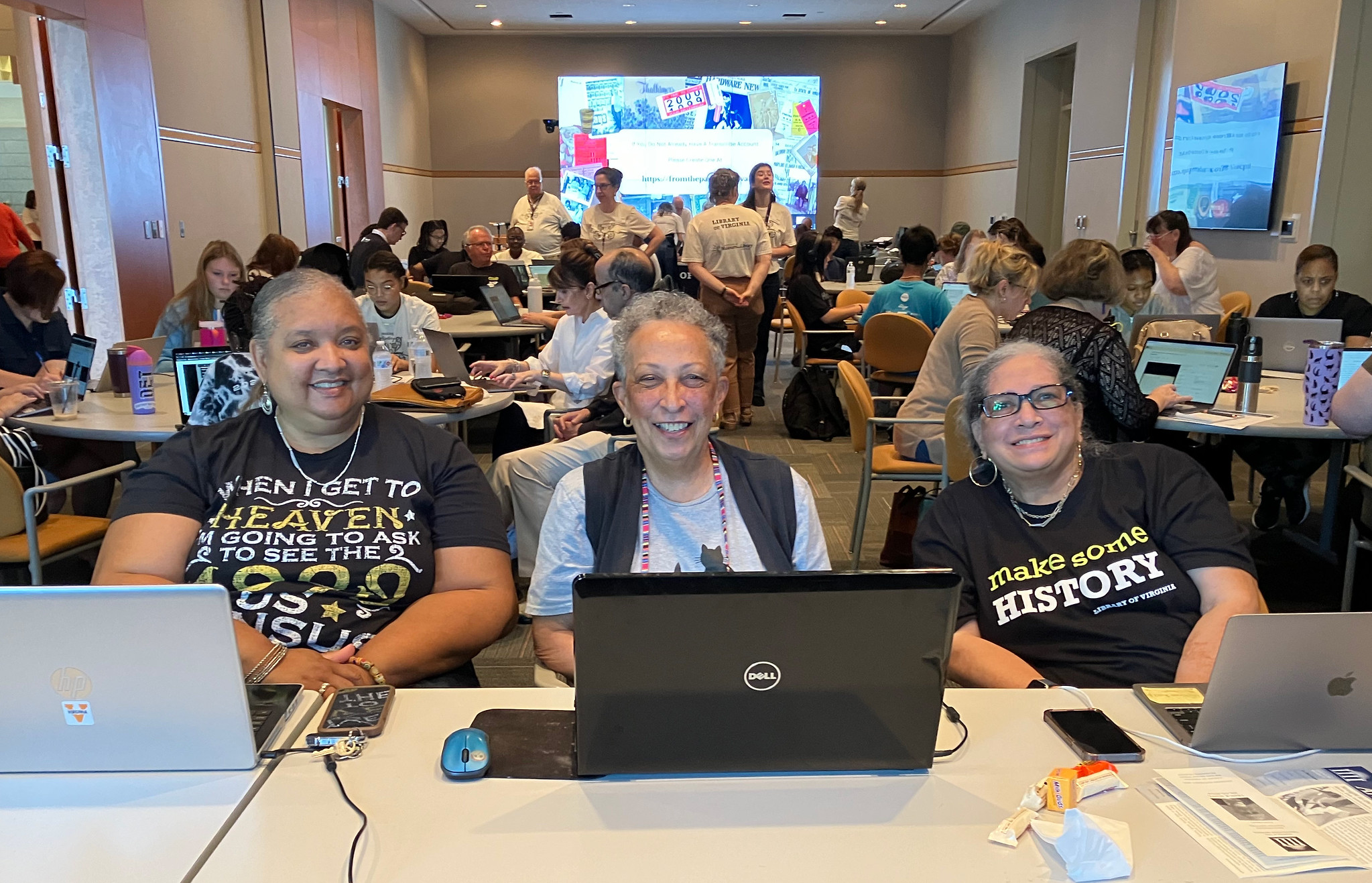 Three smiling volunteers with open laptops at Transcribe workshop