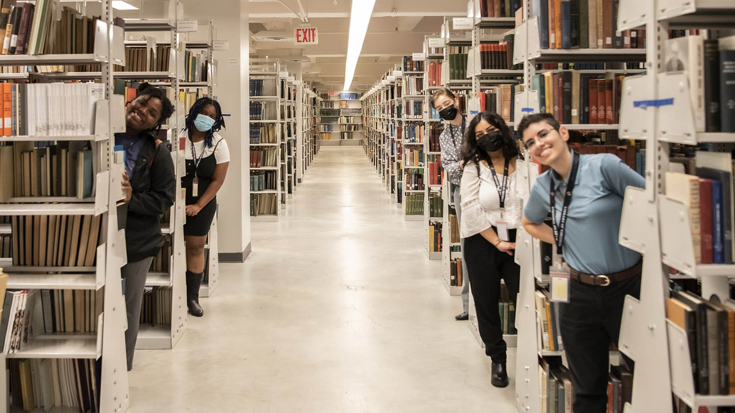Five people peek out from between bookshelves