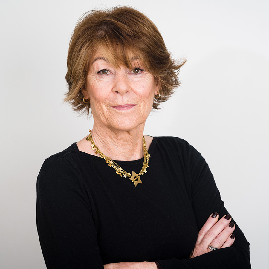 Author Sue Prideaux stands against a white background wearing a black sweater