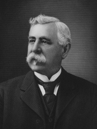 headshot of a white man with a mustache wearing late 19th century attire