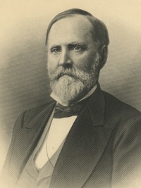 Headshot of a white man with a beard wearing late 19th century attire.