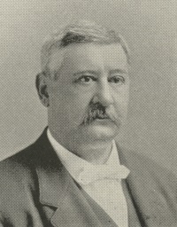Headshot of white man with a mustache wearing late 19th century attire.