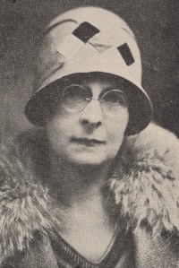 Headshot of a white woman wearing glasses, a cloche hat, and early 19th century attire.