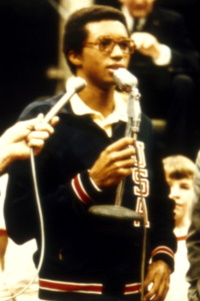 An African American man wearing a USA jacket speaking into a microphone.