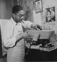 African American man holding a piece of wood that he is sculpting.
