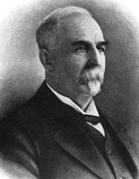 Headshot of a white man with a mustache wearing a suit.