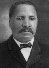 Headshot of an African American man with a mustache and wearing a suit with a bowtie.
