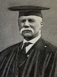 Older white man with a mustache wearing a graduation cap and gown.
