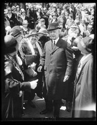 A white man in a hat and suit in the middle of a crowd.