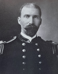 Headshot of a white man with a mustache wearing a U.S. Navy uniform.