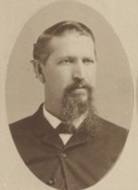 Headshot of a white man with a beard wearing late 19th century attire.