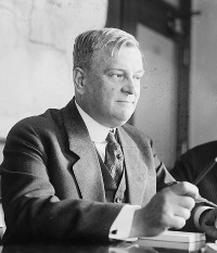 White man wearing a suit sitting at a desk.