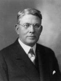 Headshot of a white man with glasses wearing a suit.