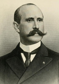 Headshot of a white man with a mustache wearing late 19th century attire.