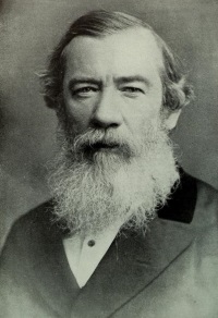 Headshot of a white man with a beard wearing late 19th century attire.