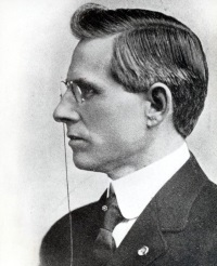 Side-view photograph of a white man wearing a pince-nez and early 20th-century suit.