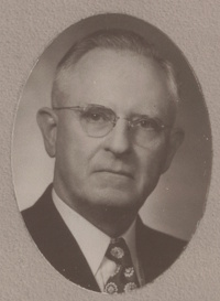Headshot of a white man with glasses wearing mid-20th century attire.