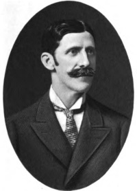 Headshot of a man with a mustache wearing a suit and tie.