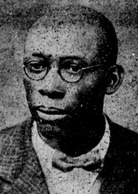 Newspaper photograph of an African American man wearing glasses and early 20th century attire.