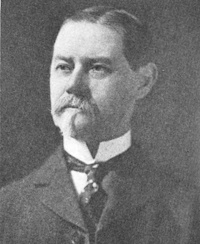 Headshot of a white man with a mustache wearing early 20th century attire.