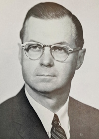 Headshot of a white man with glasses wearing mid-20th century attire.