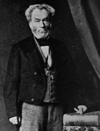 White man wearing mid-19th century attire standing with his hand on a book.