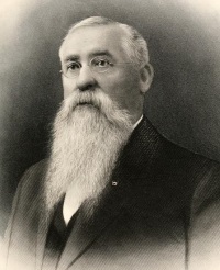 Headshot of a white man with a long white beard wearing early 20th century attire.