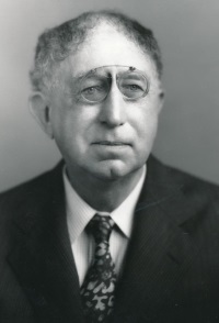 Headshot of a white man wearing a pince-nez and a suit.