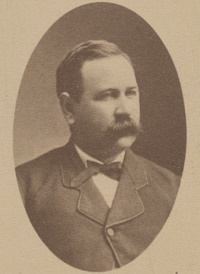 Headshot of a white man with a mustache wearing late 19th century attire.
