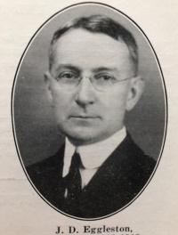 Headshot of a white man with glasses wearing early 20th century attire.