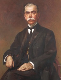Oil portrait of a seated white man with a mustache wearing early 20th century attire.