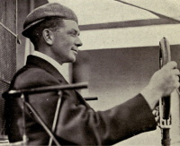 Profile photograph of a white man sitting at the controls of an early 20th century airplane.