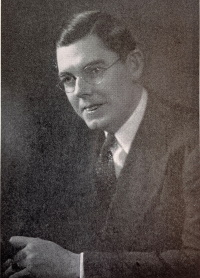 A white man with glasses wearing a mid-20th century suit and tie.