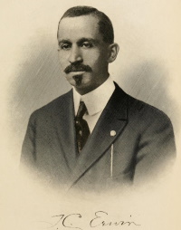 Headshot of an African American man with a mustache and goatee wearing early 20th century attire with his signature T.C. Erwin beneath.