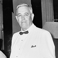 Candid photograph of a white man wearing a formal white suit.