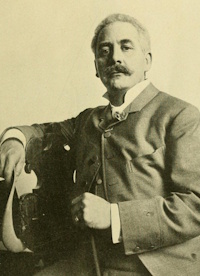 Studio photograph of a white man with a mustache seated and holding a cane.