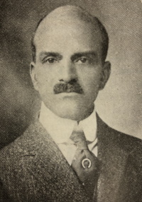 Headshot of an African American man with a mustache wearing an early 20th century suit and tie.