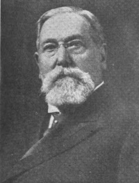 Headshot of a white man with a beard and mustache wearing late 19th century attire.