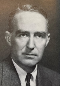 Headshot of a white man wearing a mid-20th century suit and tie.
