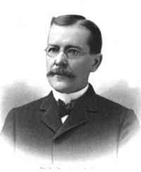 Headshot of a white man with a mustache wearing glasses and early 20th century attire.