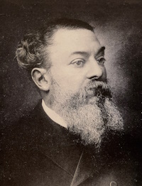 An African American man with a beard and mustache wearing a dark suit.