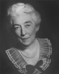 Studio portrait of a white woman wearing a black dress with lace collar and peal necklace.