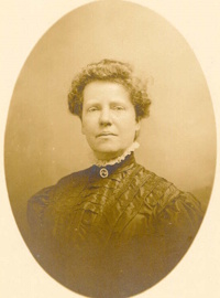 Headshot of a white woman wearing late a late 19th century dress with a cameo brooch.