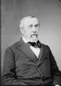 Studio photograph of a white man with a beard and mustache wearing mid-19th century attire.