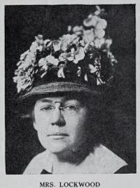 Headshot of a white woman wearing glasses and elaborate hat.