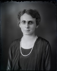 Headshot of a white woman with glasses and wearing early 20th century attire.