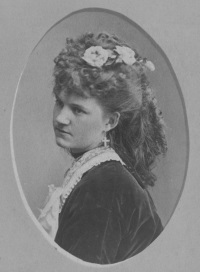 Studio photograph of a white woman with elaborate 19th century hairstyle and dress with lace collar.
