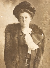 White woman wearing an early 20th century hat and fur stole.